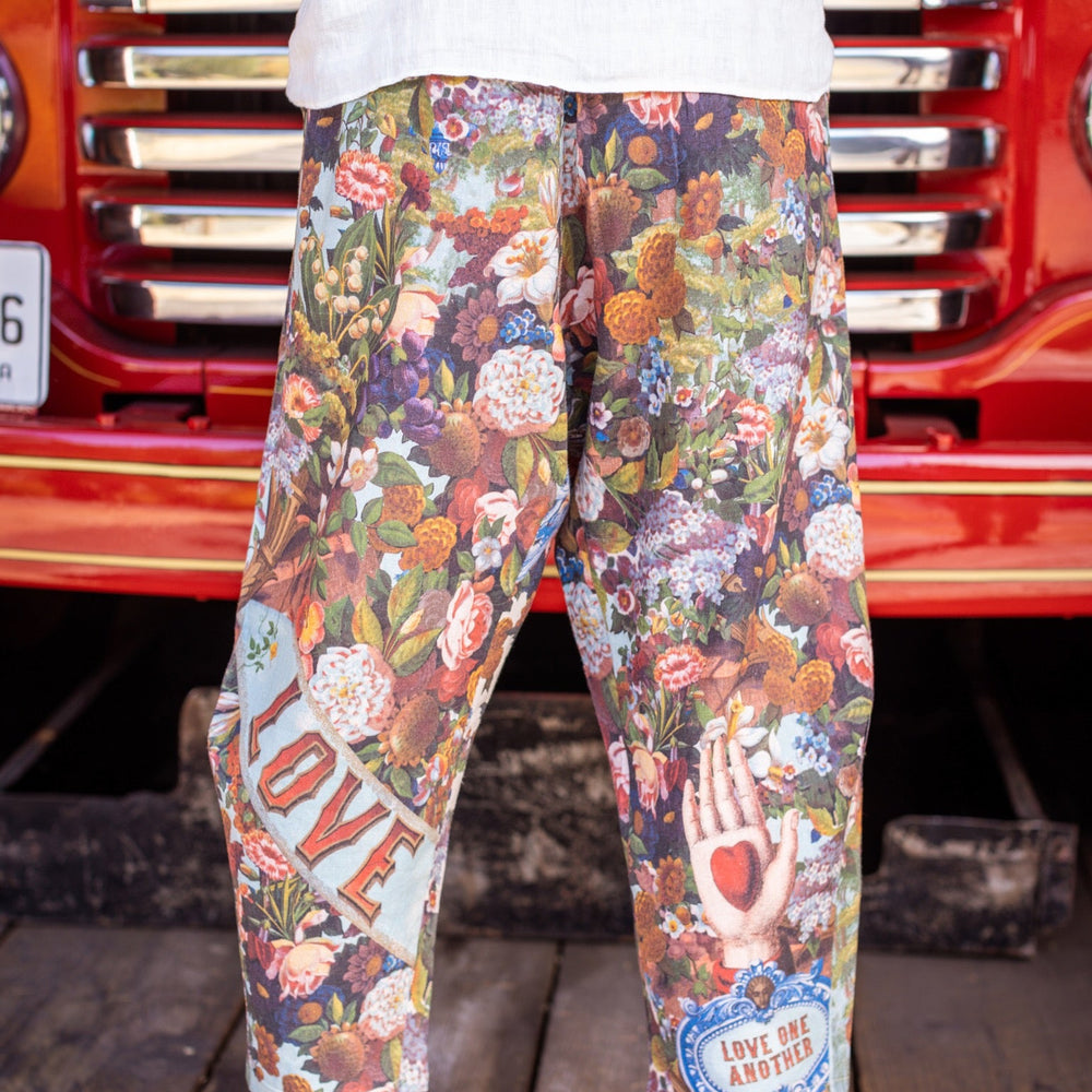 
                  
                    Model wearing linen blend artist pants with 1854 floral art, heart-in-hand symbol, and “Love one another” handwritten script – Market of Stars.
                  
                
