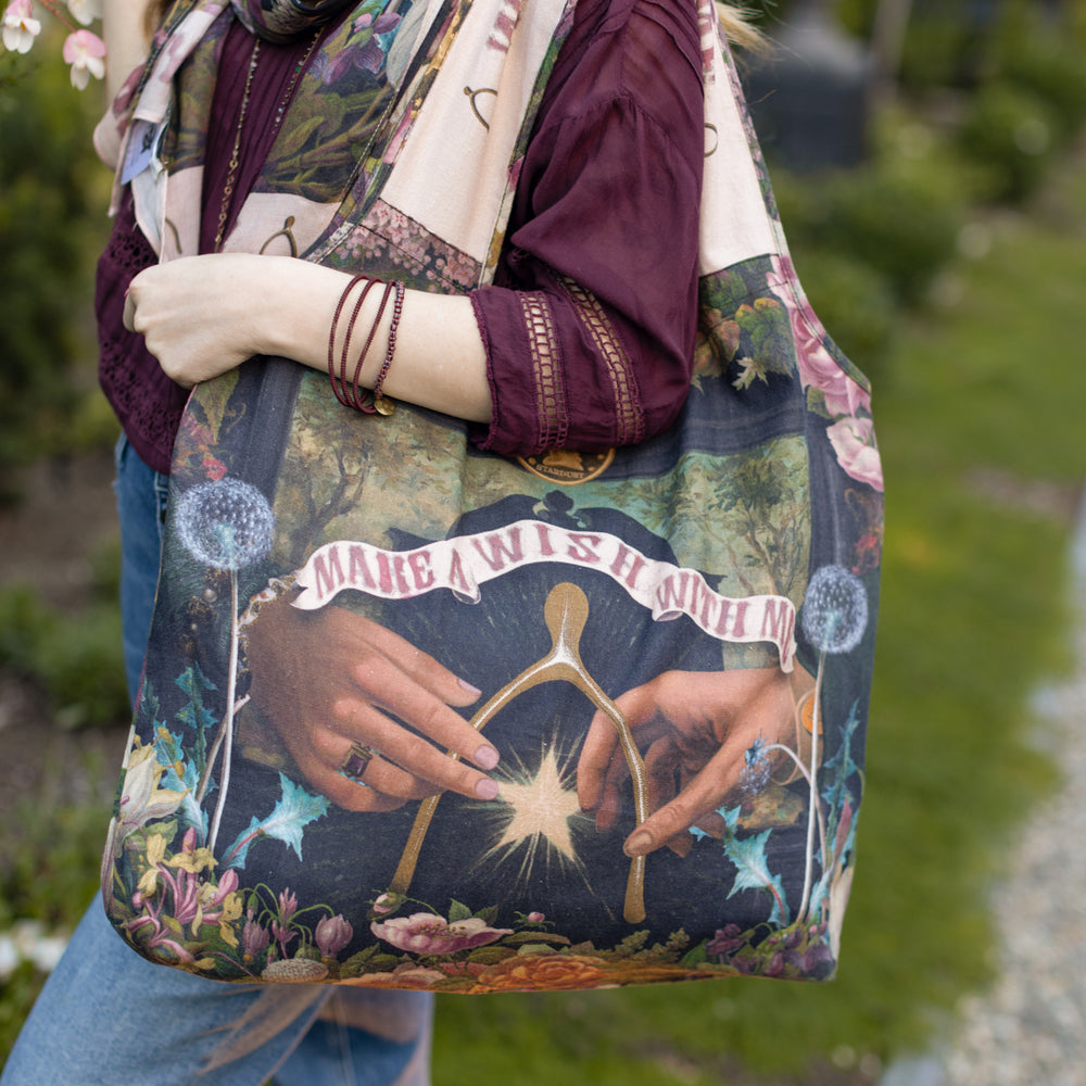 Model holding linen blend market tote featuring Victorian wishbone–vintage coin–evening star–dandelion–and “Best Wishes” banner on floral background – Market of Stars