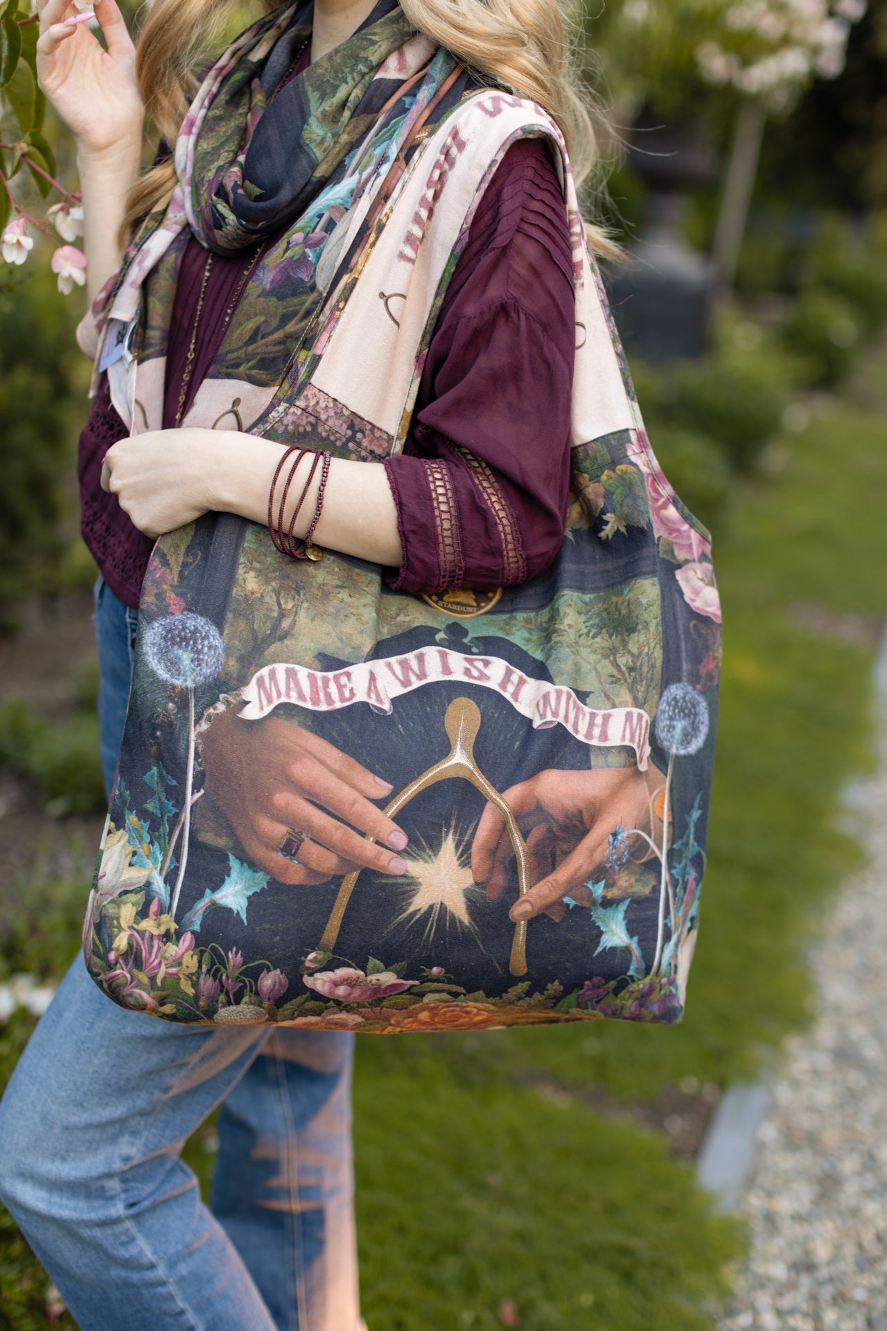 Model holding linen blend market tote featuring Victorian wishbone–vintage coin–evening star–dandelion–and “Best Wishes” banner on floral background – Market of Stars