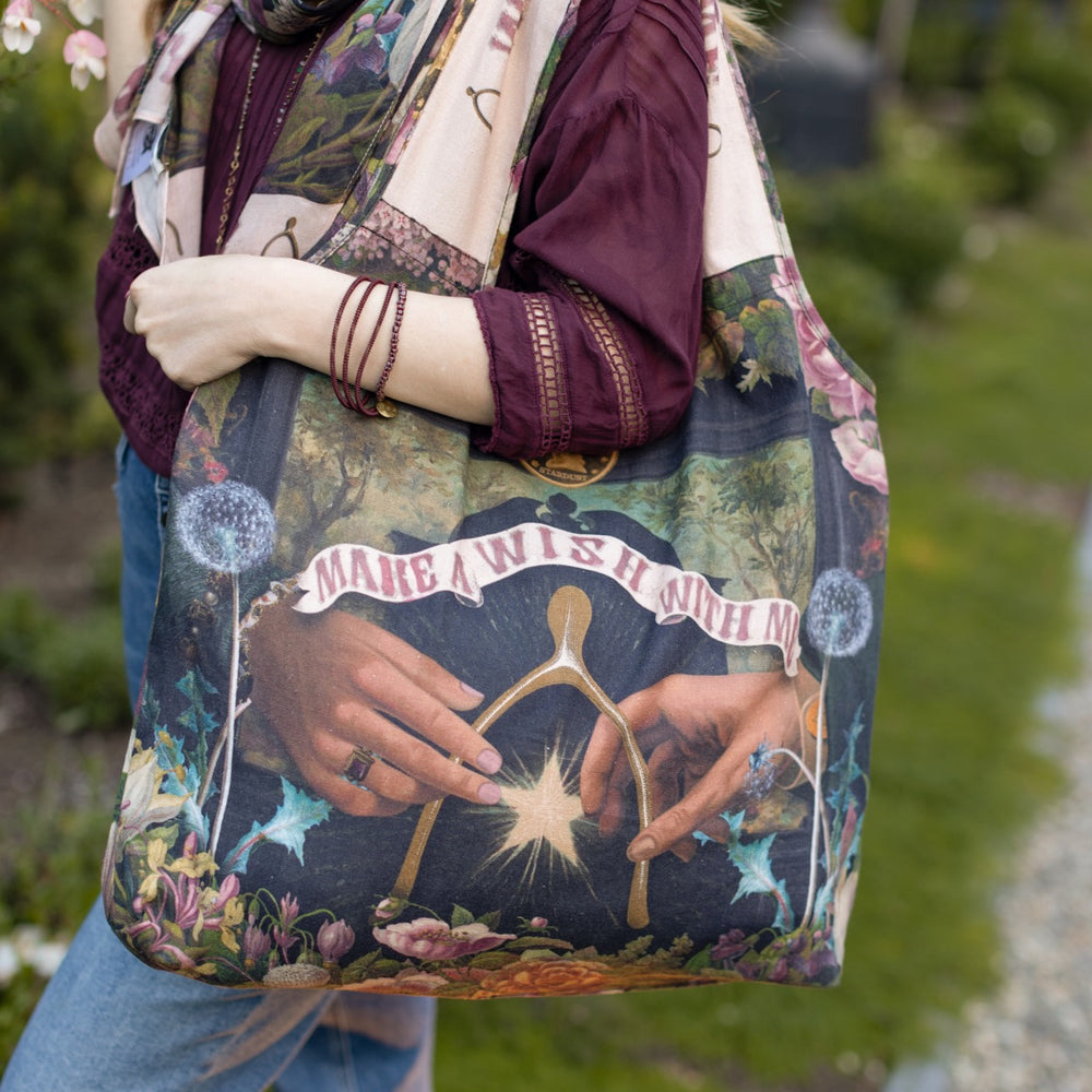 Model holding linen blend market tote featuring Victorian wishbone–vintage coin–evening star–dandelion–and “Best Wishes” banner on floral background – Market of Stars