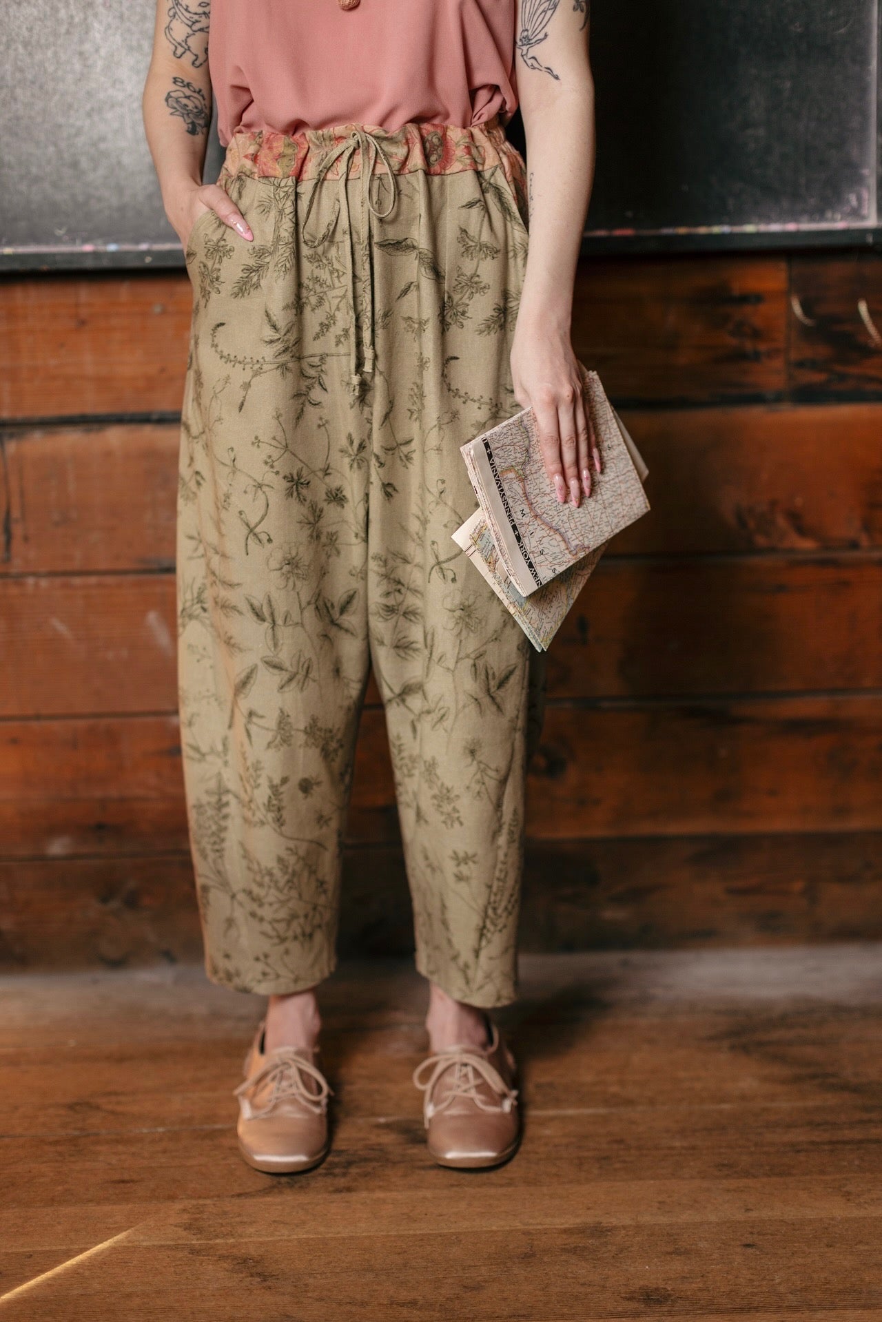 Model wearing artist pants in sage featuring reimagined vintage 1846 map of a woman’s heart with playful updated place names – Market of Stars