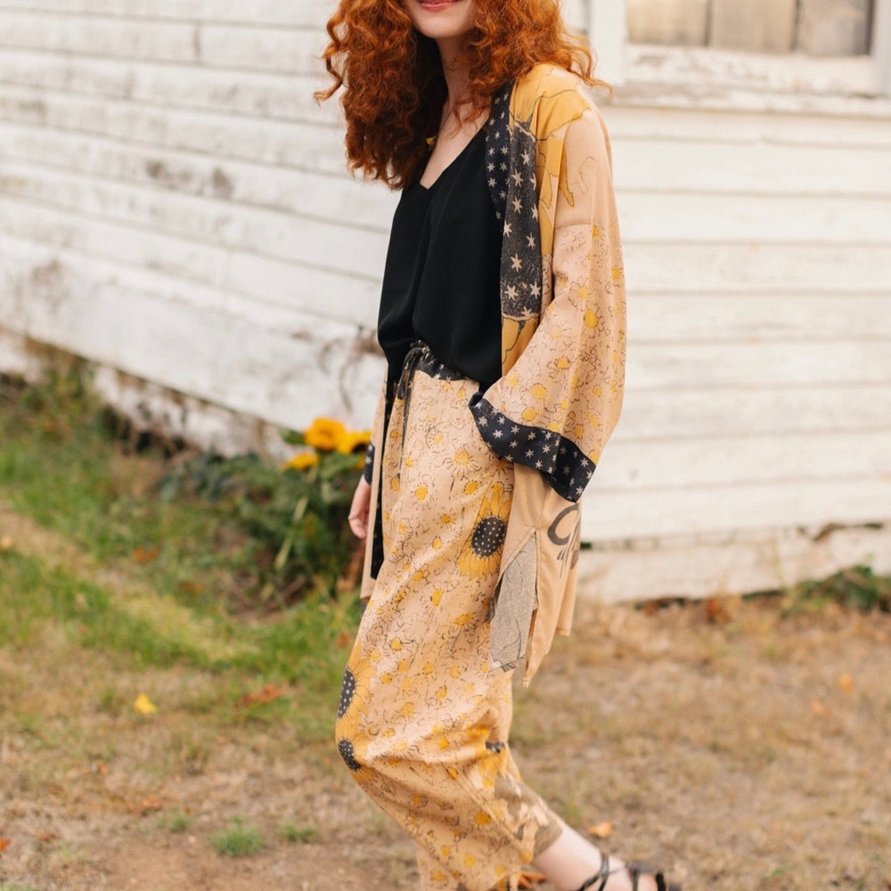 
                  
                    Model wearing the Milk & Honey Artist Pants featuring playful 1904 Brooklyn poster art and antique woodcut star and floral details in vintage-inspired tones – Market of Stars.
                  
                