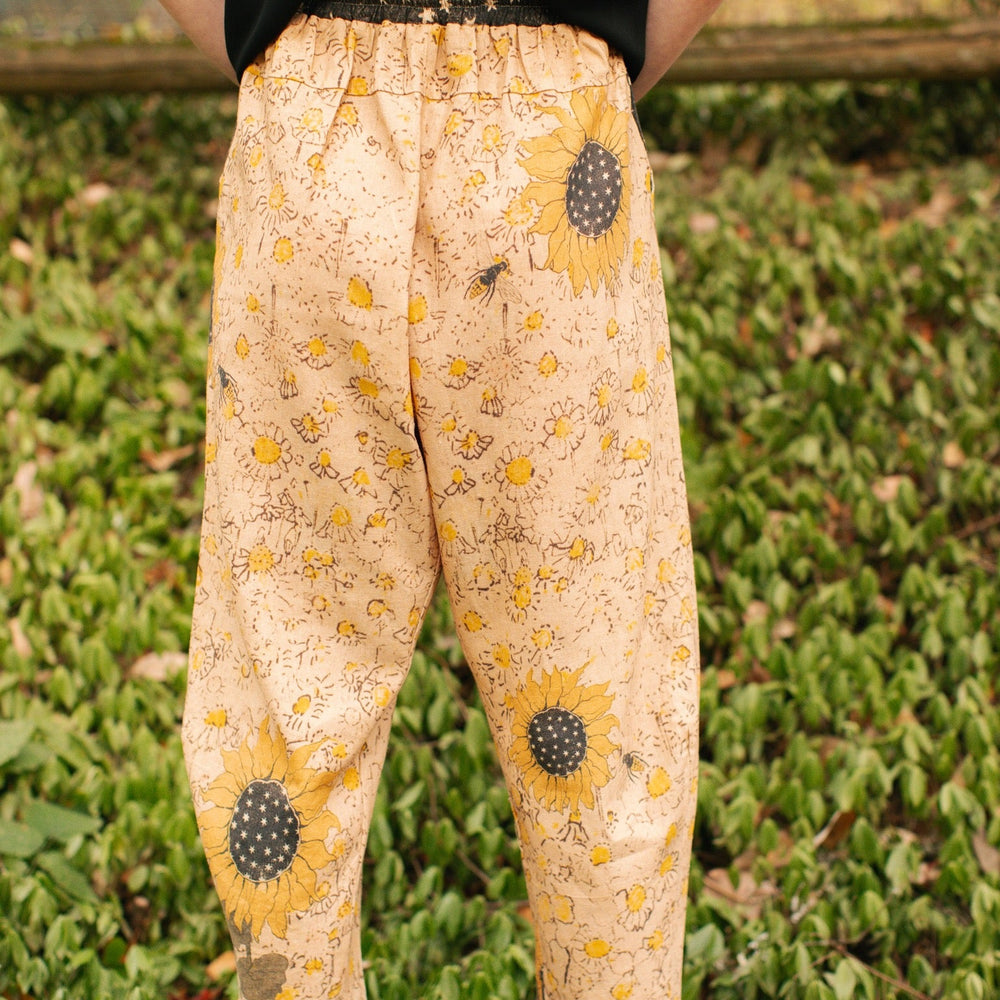 
                  
                    Model wearing the Milk & Honey Artist Pants featuring playful 1904 Brooklyn poster art and antique woodcut star and floral details in vintage-inspired tones – Market of Stars.
                  
                