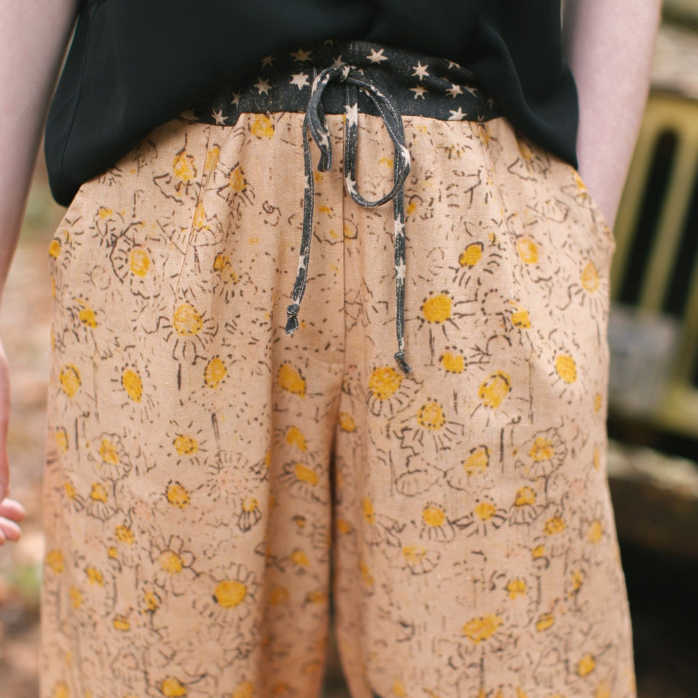 
                  
                    Model wearing the Milk & Honey Artist Pants featuring playful 1904 Brooklyn poster art and antique woodcut star and floral details in vintage-inspired tones – Market of Stars.
                  
                