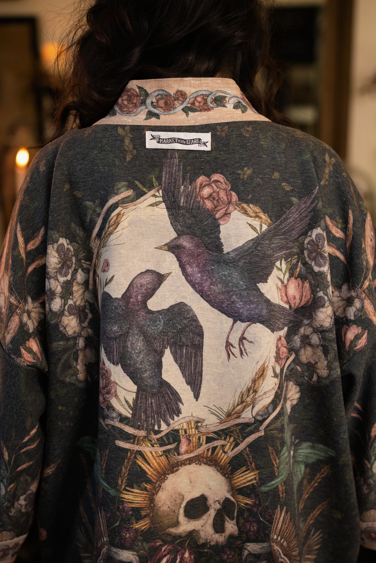 Model wearing a cozy fleece lined cottage cardigan ft. artwork created by Jessica Roux including two starlings beneath a full moon with flowers, butterflies, moths and botanical artwork - Market of Stars