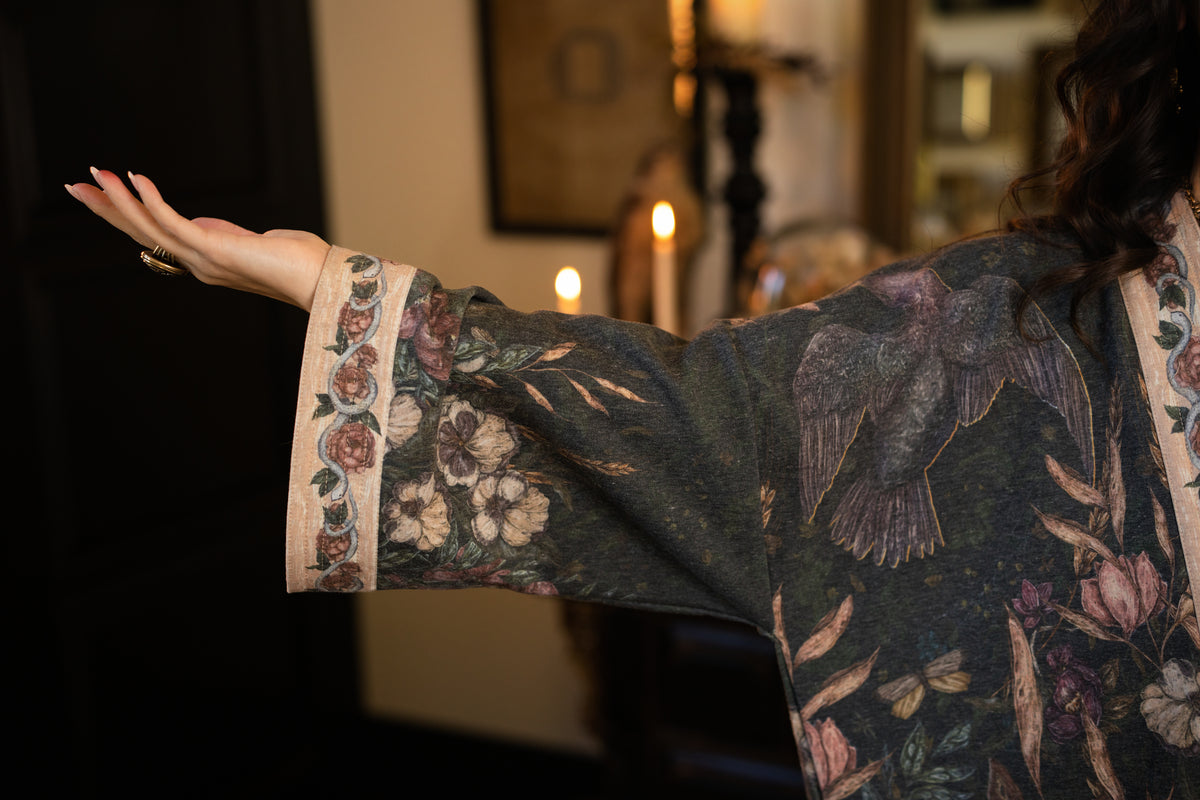 Model wearing a cozy fleece lined cottage cardigan ft. artwork created by Jessica Roux including two starlings beneath a full moon with flowers, butterflies, moths and botanical artwork - Market of Stars