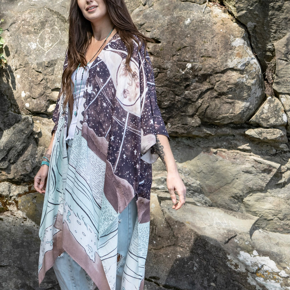 
                  
                    Model wearing Moonstruck Goddess Duster featuring original artwork by Leslie Love, inspired by the ocean, the night sky, and the artist’s handmade botanical inks – Market of Stars.
                  
                