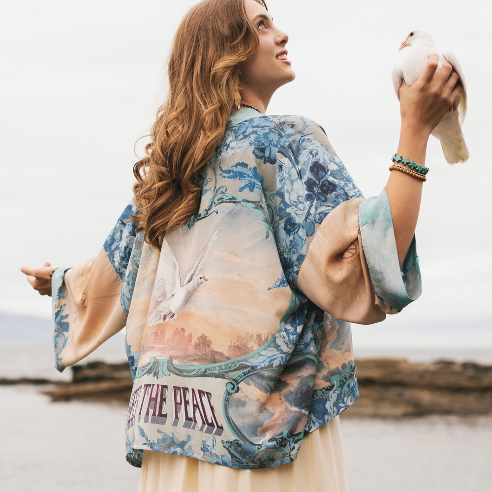 Model wearing our Peace Out Pixie Duster featuring 1800's perfumeur sign with gentle tones of blue & aqua, landscapes, clouds, dove and peace symbols -Market of Stars.