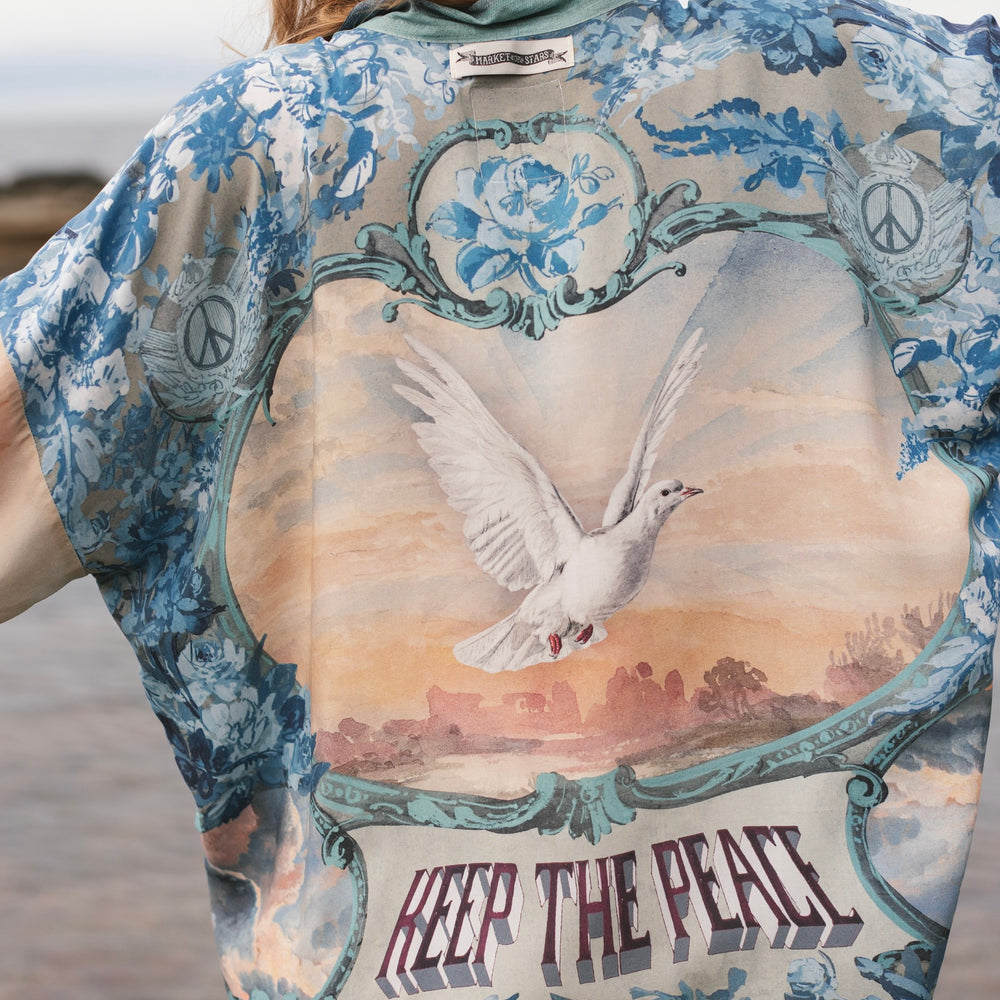 
                  
                    Model wearing our Peace Out Pixie Duster featuring 1800's perfumeur sign with gentle tones of blue & aqua, landscapes, clouds, dove and peace symbols -Market of Stars.
                  
                