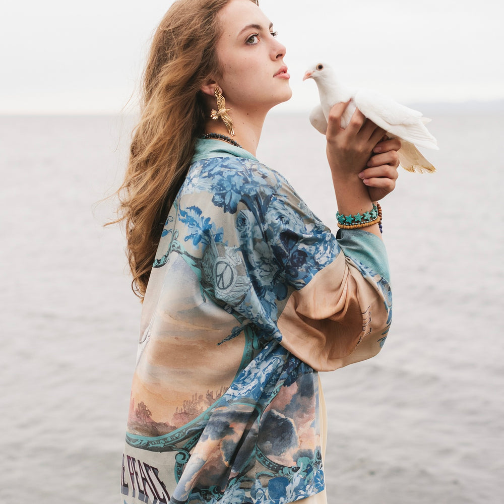 
                  
                    Model wearing our Peace Out Pixie Duster featuring 1800's perfumeur sign with gentle tones of blue & aqua, landscapes, clouds, dove and peace symbols -Market of Stars.
                  
                
