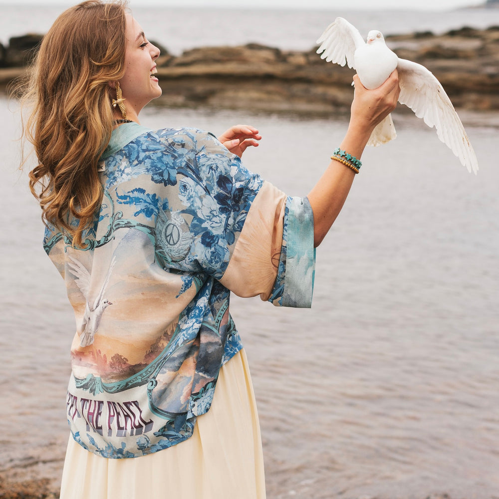 
                  
                    Model wearing our Peace Out Pixie Duster featuring 1800's perfumeur sign with gentle tones of blue & aqua, landscapes, clouds, dove and peace symbols -Market of Stars.
                  
                