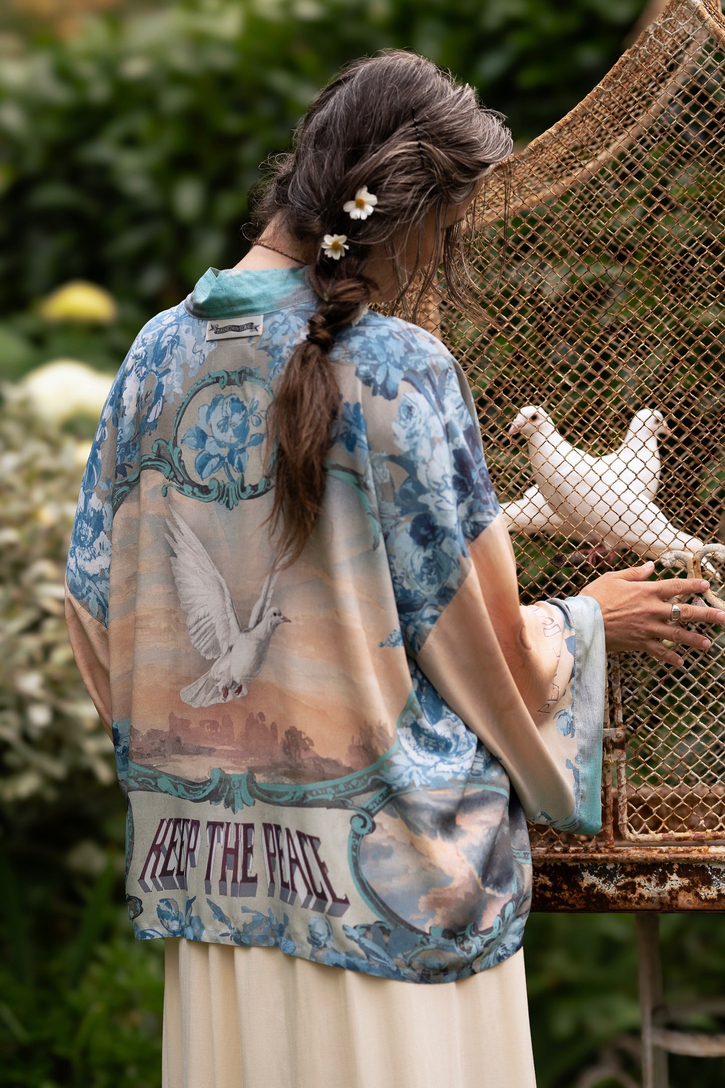 Model wearing our Peace Out Pixie Duster featuring 1800's perfumeur sign with gentle tones of blue & aqua, landscapes, clouds, dove and peace symbols -Market of Stars.