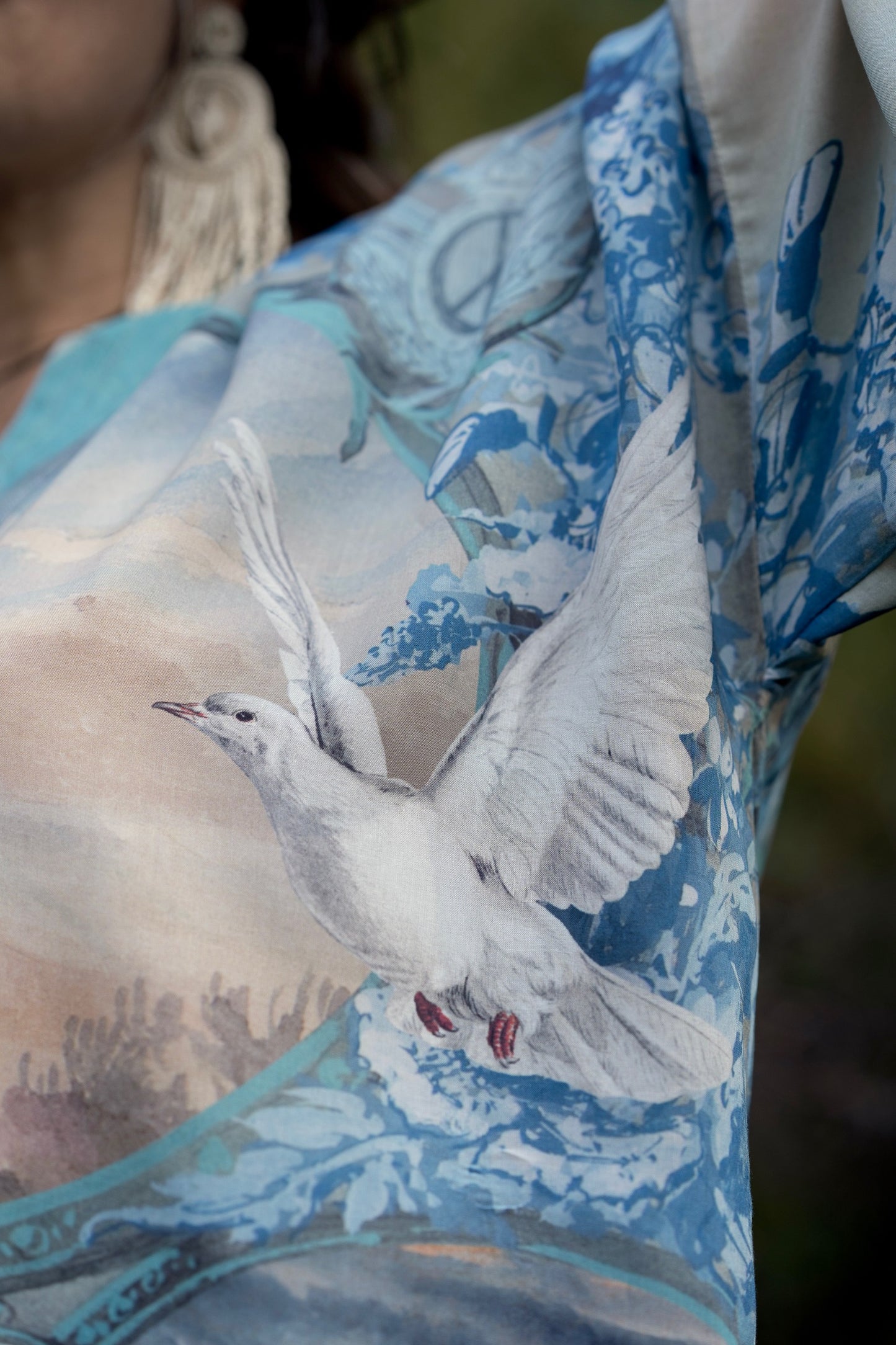 Model wearing our Peace Out Pixie Duster featuring 1800's perfumeur sign with gentle tones of blue & aqua, landscapes, clouds, dove and peace symbols -Market of Stars.
