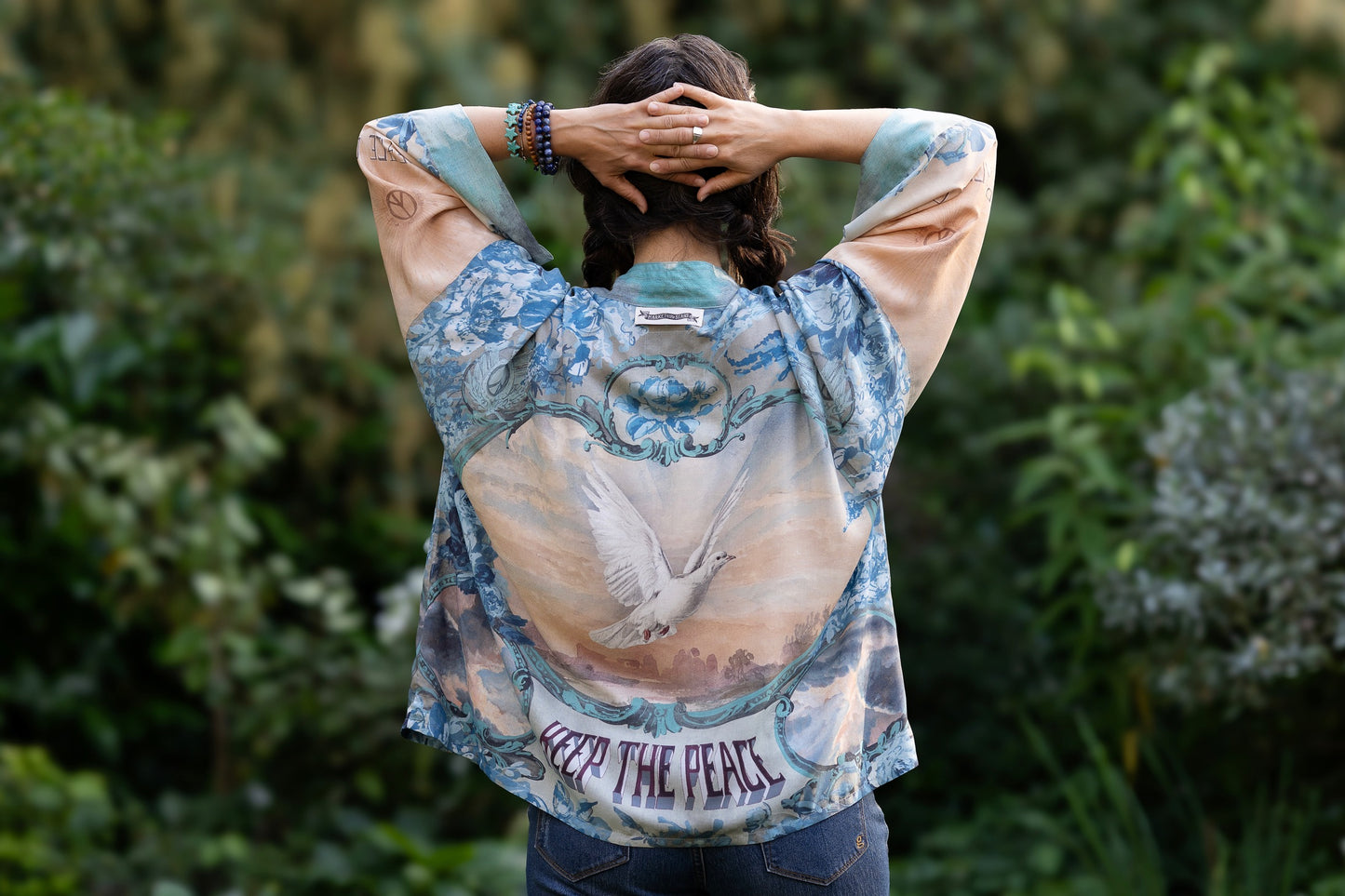 Model wearing our Peace Out Pixie Duster featuring 1800's perfumeur sign with gentle tones of blue & aqua, landscapes, clouds, dove and peace symbols -Market of Stars.
