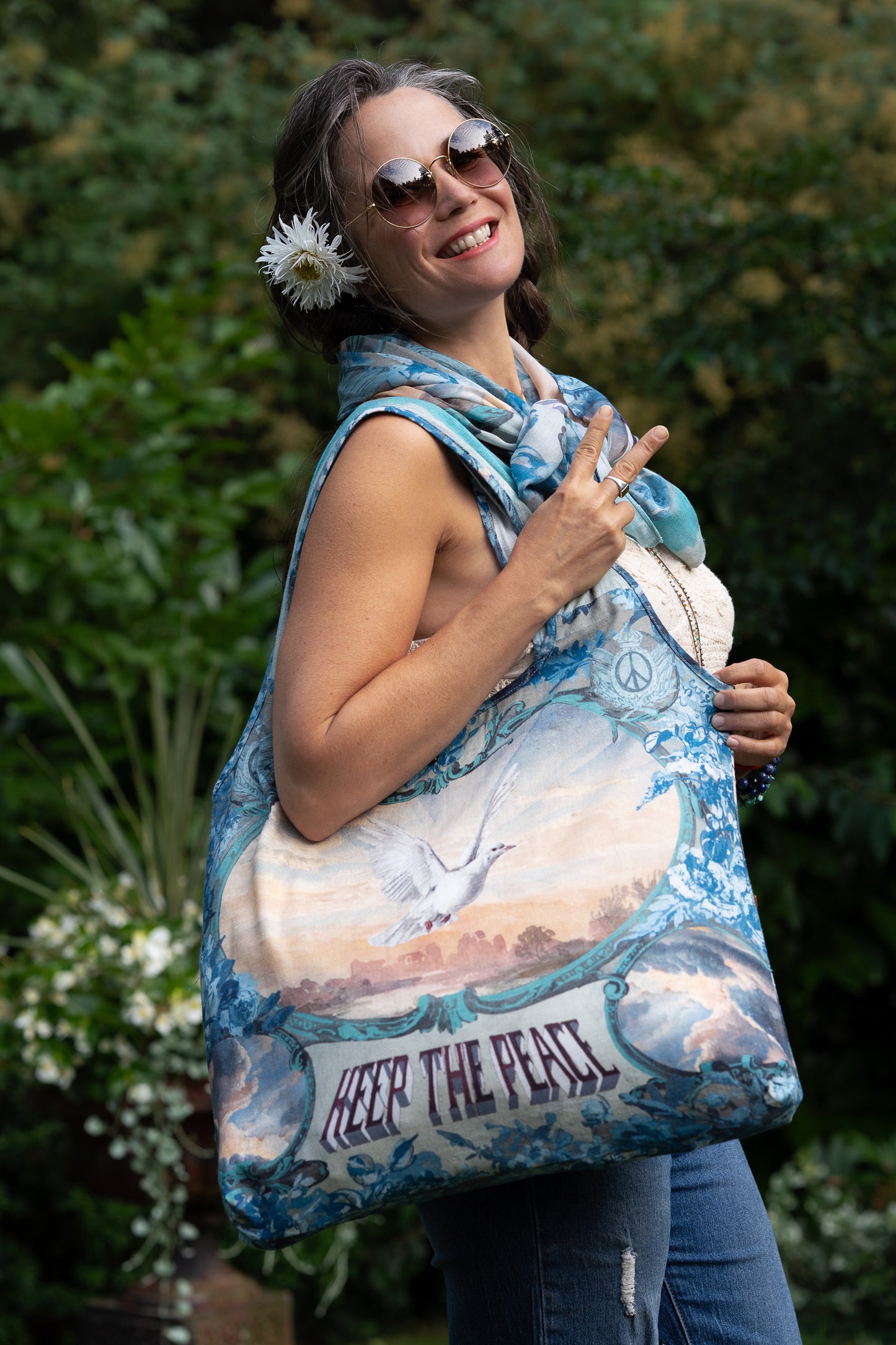Model wearing our Peace Out tote bag featuring 1800's perfumeur sign with gentle tones of blue & aqua, landscapes, clouds, dove, and peace symbols -Market of Stars.