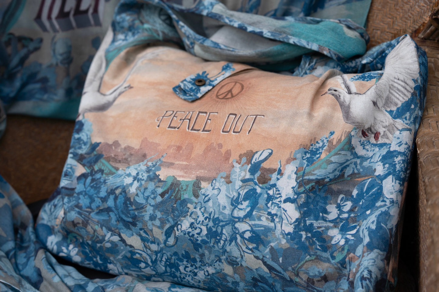 Model wearing our Peace Out tote bag featuring 1800's perfumeur sign with gentle tones of blue & aqua, landscapes, clouds, dove, and peace symbols -Market of Stars.