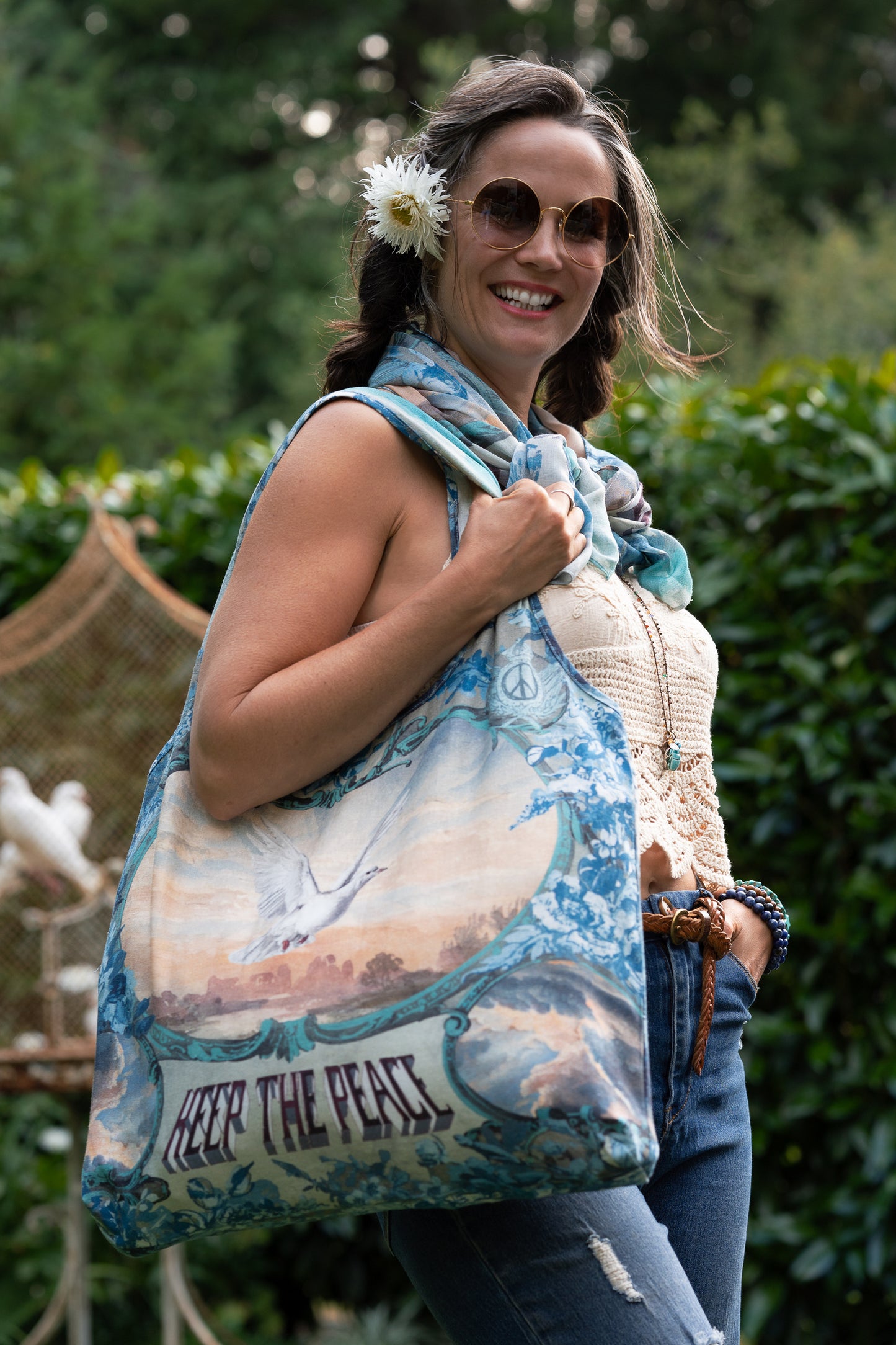 Model wearing our Peace Out tote bag featuring 1800's perfumeur sign with gentle tones of blue & aqua, landscapes, clouds, dove, and peace symbols -Market of Stars.