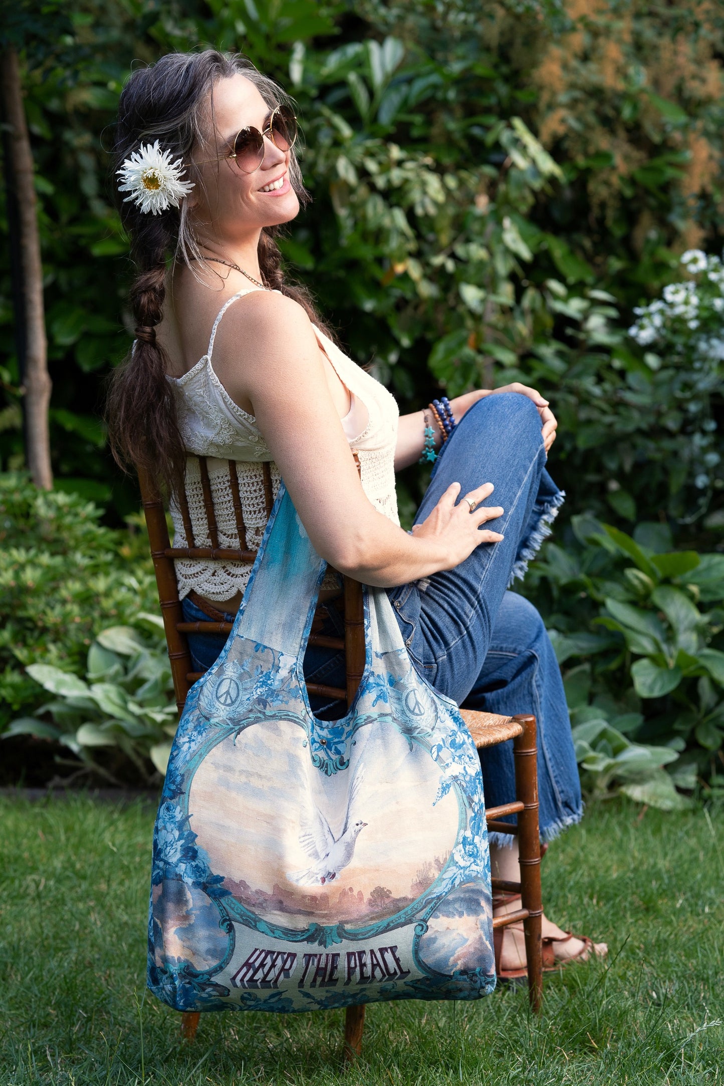 Model wearing our Peace Out tote bag featuring 1800's perfumeur sign with gentle tones of blue & aqua, landscapes, clouds, dove, and peace symbols -Market of Stars.