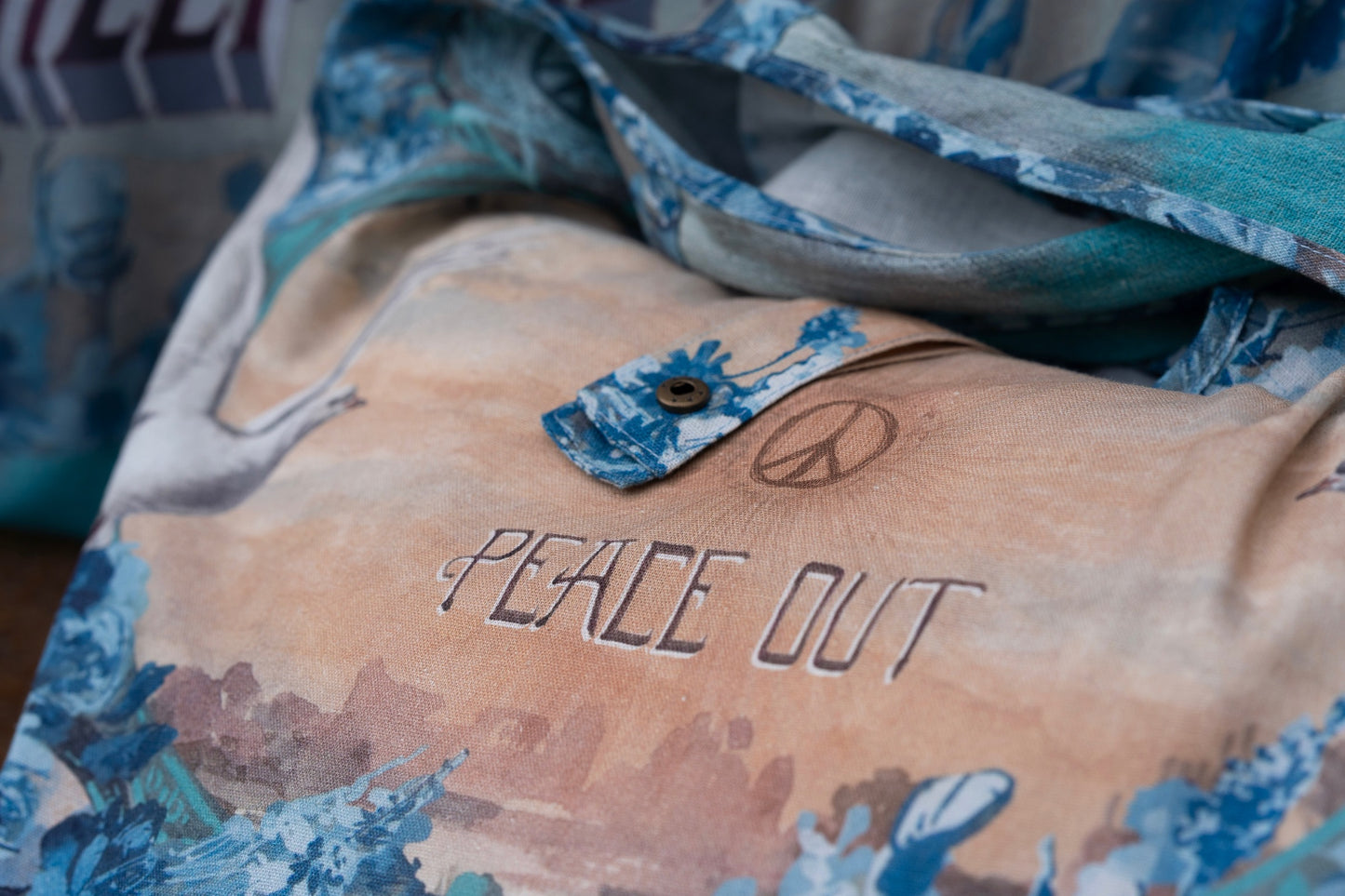 Model wearing our Peace Out tote bag featuring 1800's perfumeur sign with gentle tones of blue & aqua, landscapes, clouds, dove, and peace symbols -Market of Stars.