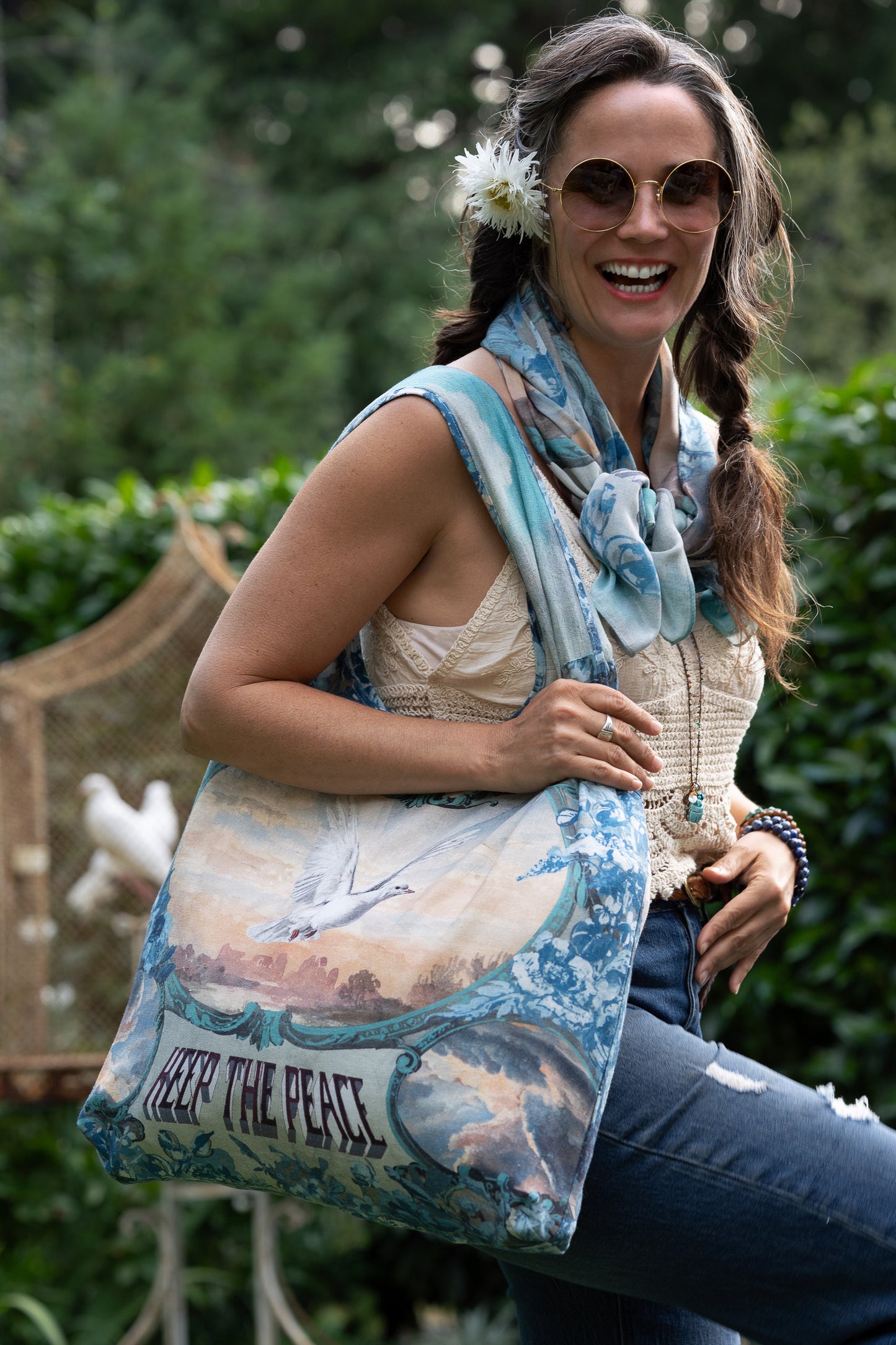 Model wearing our Peace Out tote bag featuring 1800's perfumeur sign with gentle tones of blue & aqua, landscapes, clouds, dove, and peace symbols -Market of Stars.