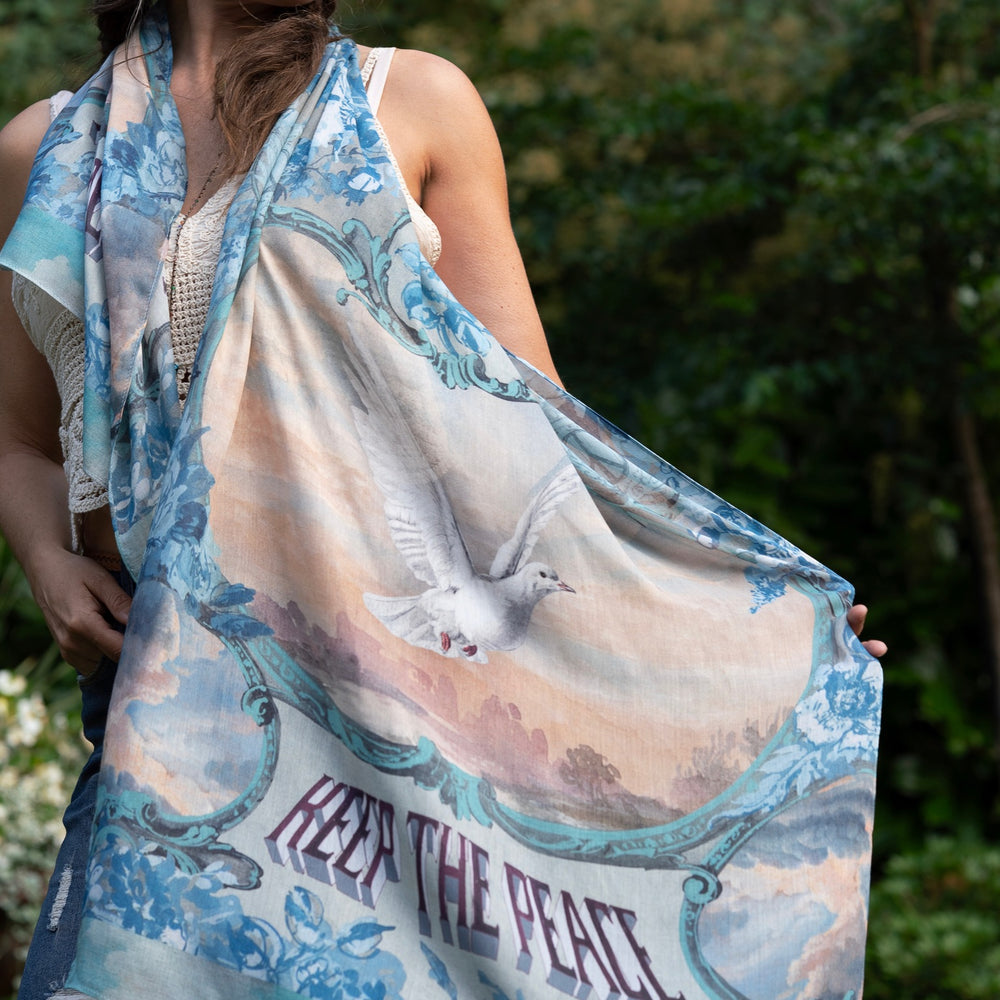 Model wearing our Peace Out scarf featuring 1800's perfumeur sign with gentle tones of blue & aqua, landscapes, clouds, dove, and peace symbols -Market of Stars