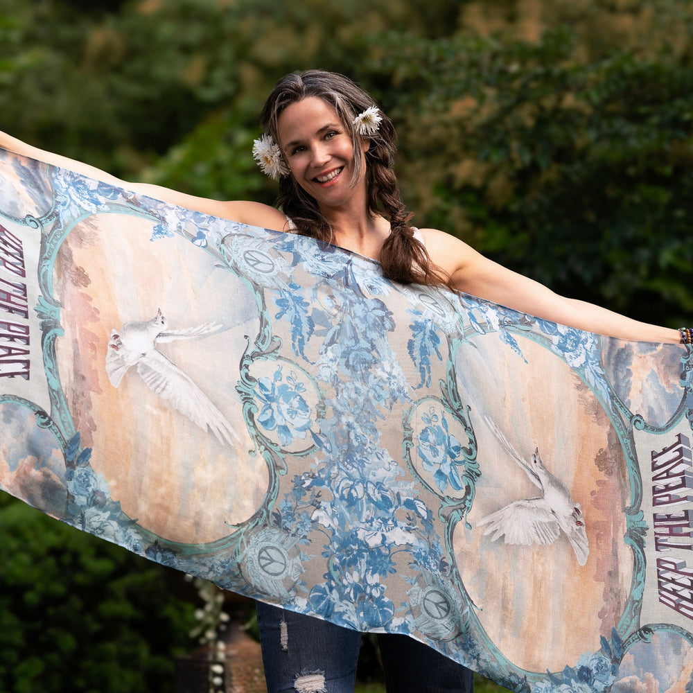 Model wearing our Peace Out scarf featuring 1800's perfumeur sign with gentle tones of blue & aqua, landscapes, clouds, dove, and peace symbols -Market of Stars