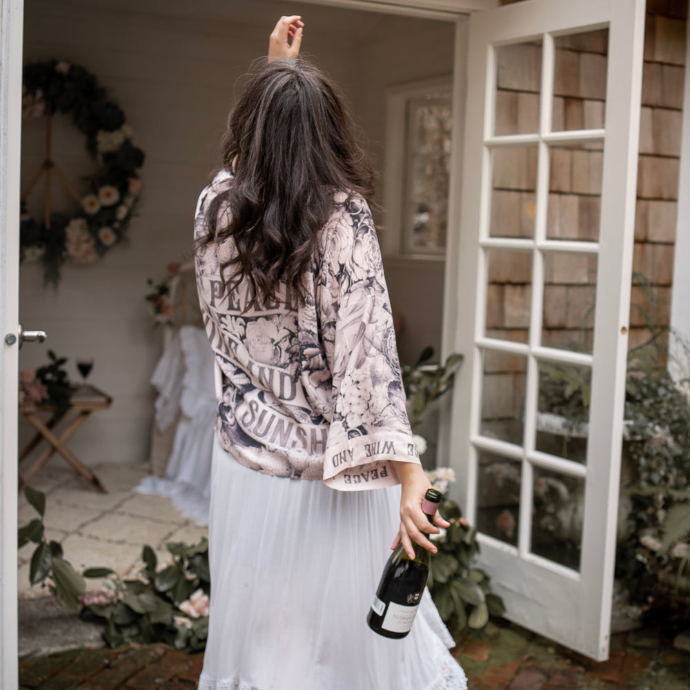 
                  
                    Model wearing Peace, Wine & Sunshine Bohéme Slip Dress featuring botanical collages and playful peace, wine and sunshine lettering on the hem – Market of Stars.
                  
                