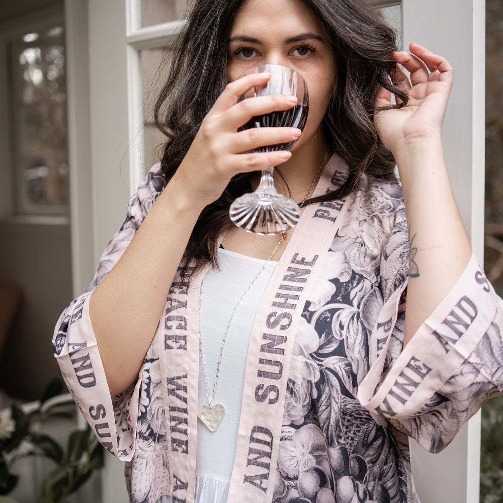 
                  
                    Model wearing Peace, Wine & Sunshine Bohéme Slip Dress featuring botanical collages and playful peace, wine and sunshine lettering on the hem – Market of Stars.
                  
                