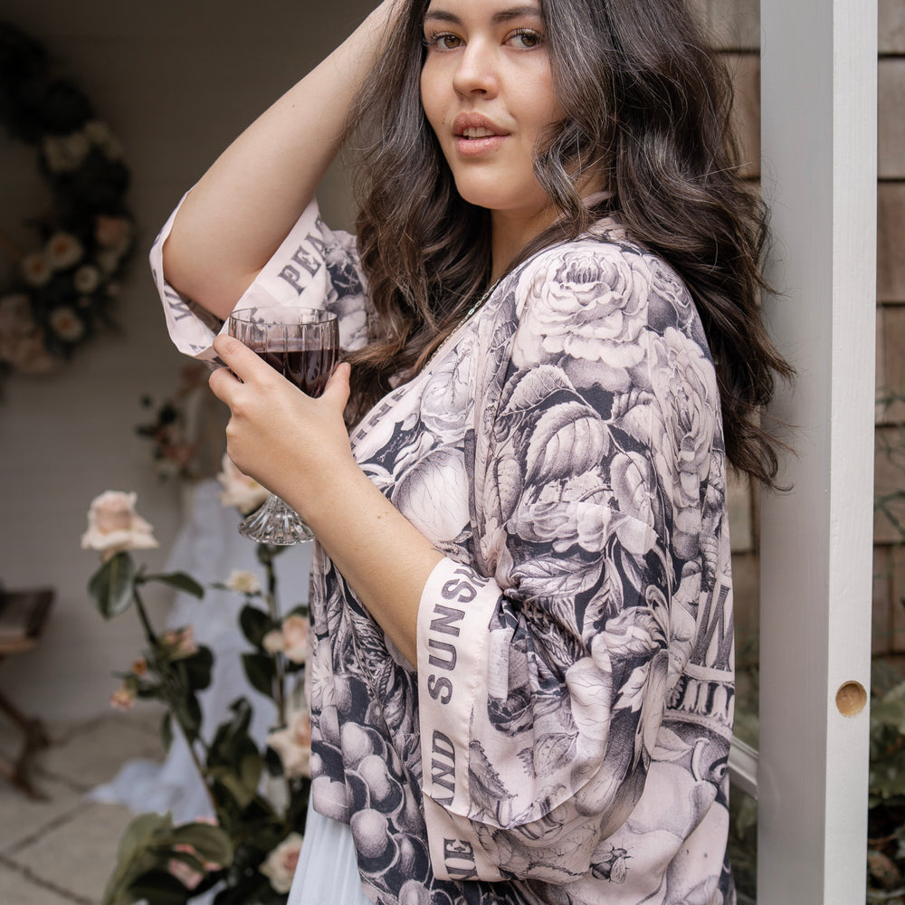 
                  
                    Model wearing Peace, Wine & Sunshine Bohéme Slip Dress featuring botanical collages and playful peace, wine and sunshine lettering on the hem – Market of Stars.
                  
                