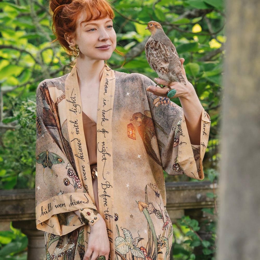 
                  
                    Model wearing an enchanting kimono duster robe featuring illustrations by Charles van Sandwyck's, crafted from airy bamboo-based viscose with a touch of whimsical magic - Market of Stars
                  
                