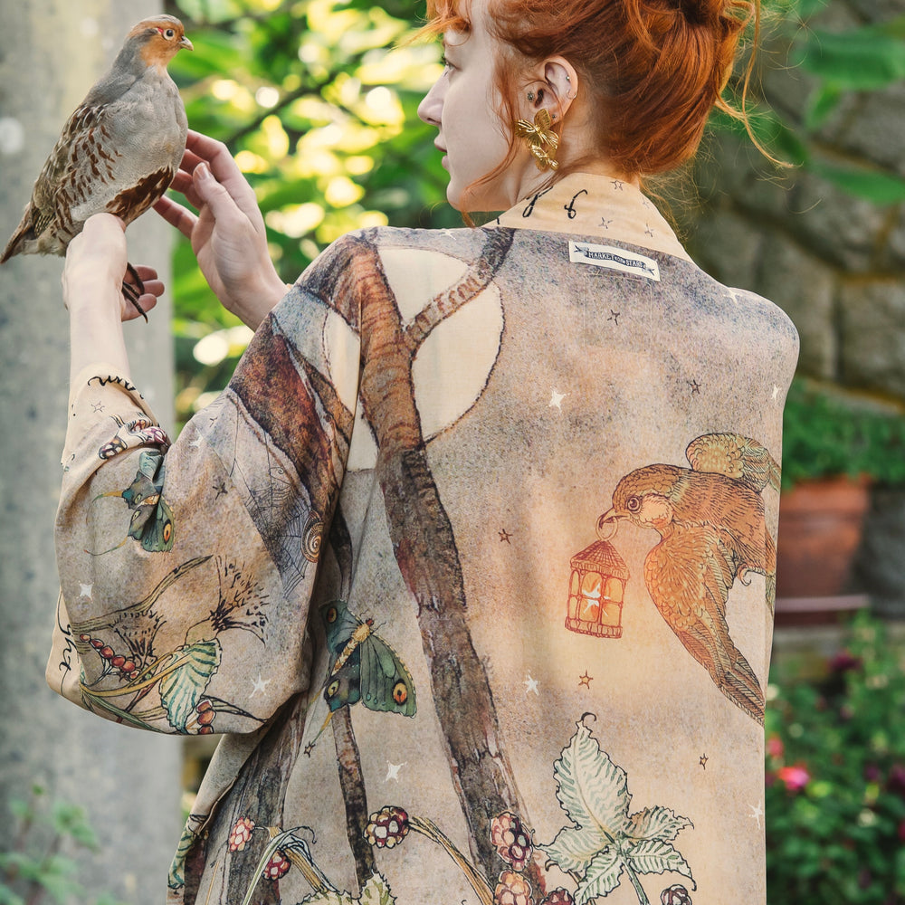 
                  
                    Model wearing an enchanting kimono duster robe featuring illustrations by Charles van Sandwyck's, crafted from airy bamboo-based viscose with a touch of whimsical magic - Market of Stars
                  
                