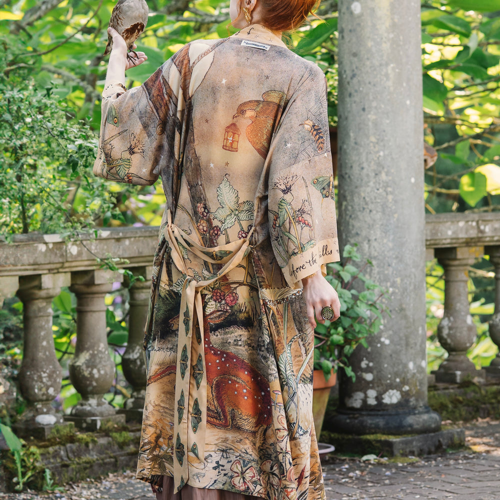 
                  
                    Model wearing an enchanting kimono duster robe featuring illustrations by Charles van Sandwyck's, crafted from airy bamboo-based viscose with a touch of whimsical magic - Market of Stars
                  
                