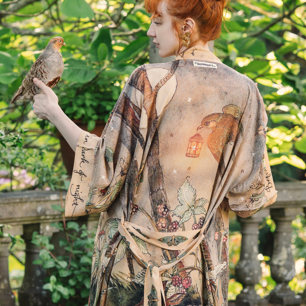 
                  
                    Model wearing an enchanting kimono duster robe featuring illustrations by Charles van Sandwyck's, crafted from airy bamboo-based viscose with a touch of whimsical magic - Market of Stars
                  
                