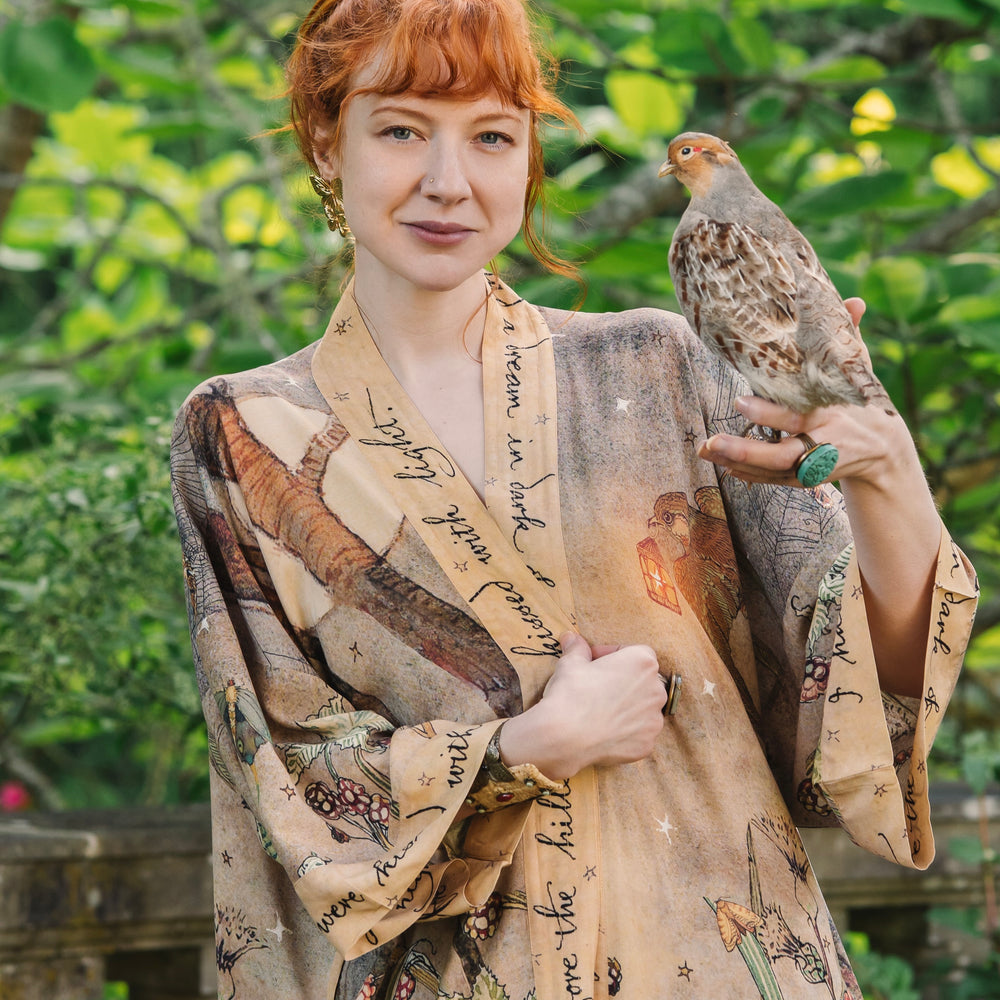 
                  
                    Model wearing an enchanting kimono duster robe featuring illustrations by Charles van Sandwyck's, crafted from airy bamboo-based viscose with a touch of whimsical magic - Market of Stars
                  
                