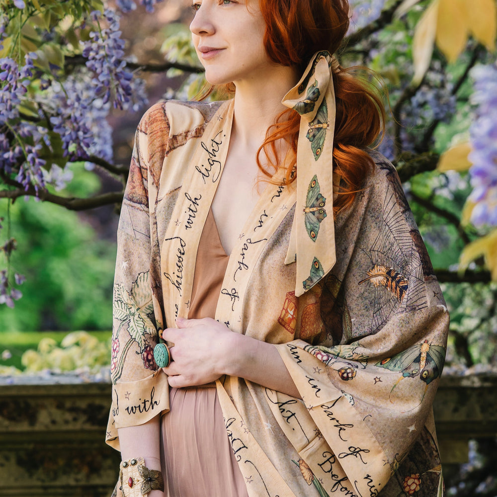 
                  
                    Model wearing an enchanting kimono duster robe featuring illustrations by Charles van Sandwyck's, crafted from airy bamboo-based viscose with a touch of whimsical magic - Market of Stars
                  
                