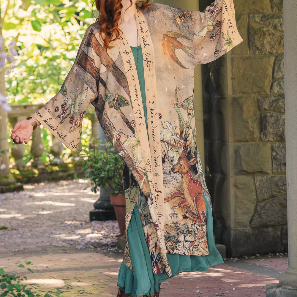 
                  
                    Model wearing an enchanting kimono duster robe featuring illustrations by Charles van Sandwyck's, crafted from airy bamboo-based viscose with a touch of whimsical magic - Market of Stars
                  
                