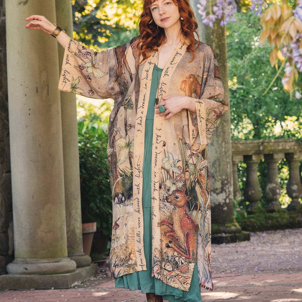 
                  
                    Model wearing an enchanting kimono duster robe featuring illustrations by Charles van Sandwyck's, crafted from airy bamboo-based viscose with a touch of whimsical magic - Market of Stars
                  
                
