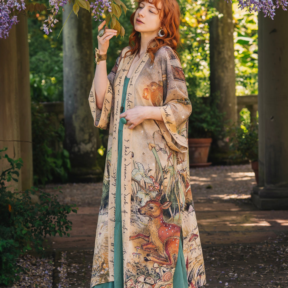 
                  
                    Model wearing an enchanting kimono duster robe featuring illustrations by Charles van Sandwyck's, crafted from airy bamboo-based viscose with a touch of whimsical magic - Market of Stars
                  
                