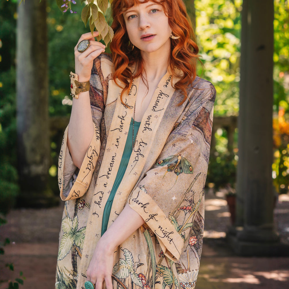 
                  
                    Model wearing an enchanting kimono duster robe featuring illustrations by Charles van Sandwyck's, crafted from airy bamboo-based viscose with a touch of whimsical magic - Market of Stars
                  
                