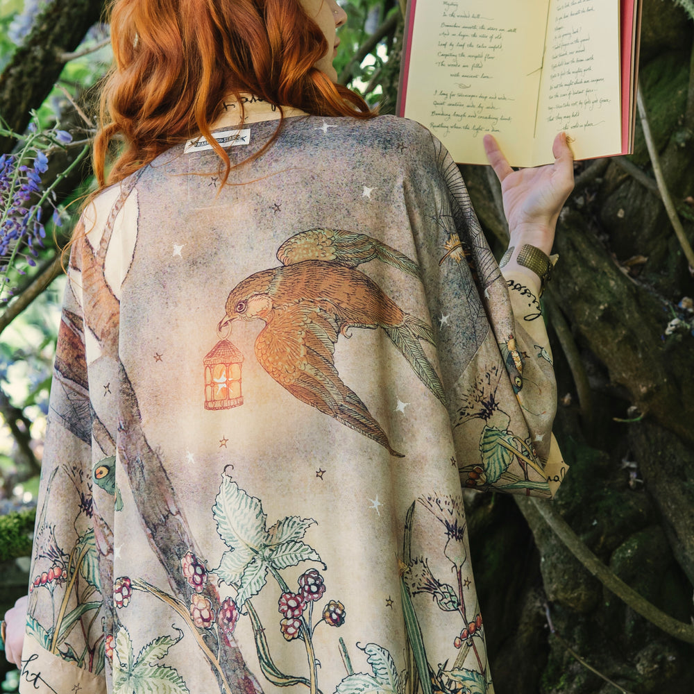
                  
                    Model wearing an enchanting kimono duster robe featuring illustrations by Charles van Sandwyck's, crafted from airy bamboo-based viscose with a touch of whimsical magic - Market of Stars
                  
                