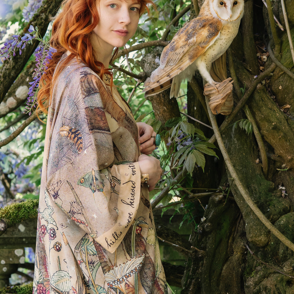 
                  
                    Model wearing an enchanting kimono duster robe featuring illustrations by Charles van Sandwyck's, crafted from airy bamboo-based viscose with a touch of whimsical magic - Market of Stars
                  
                