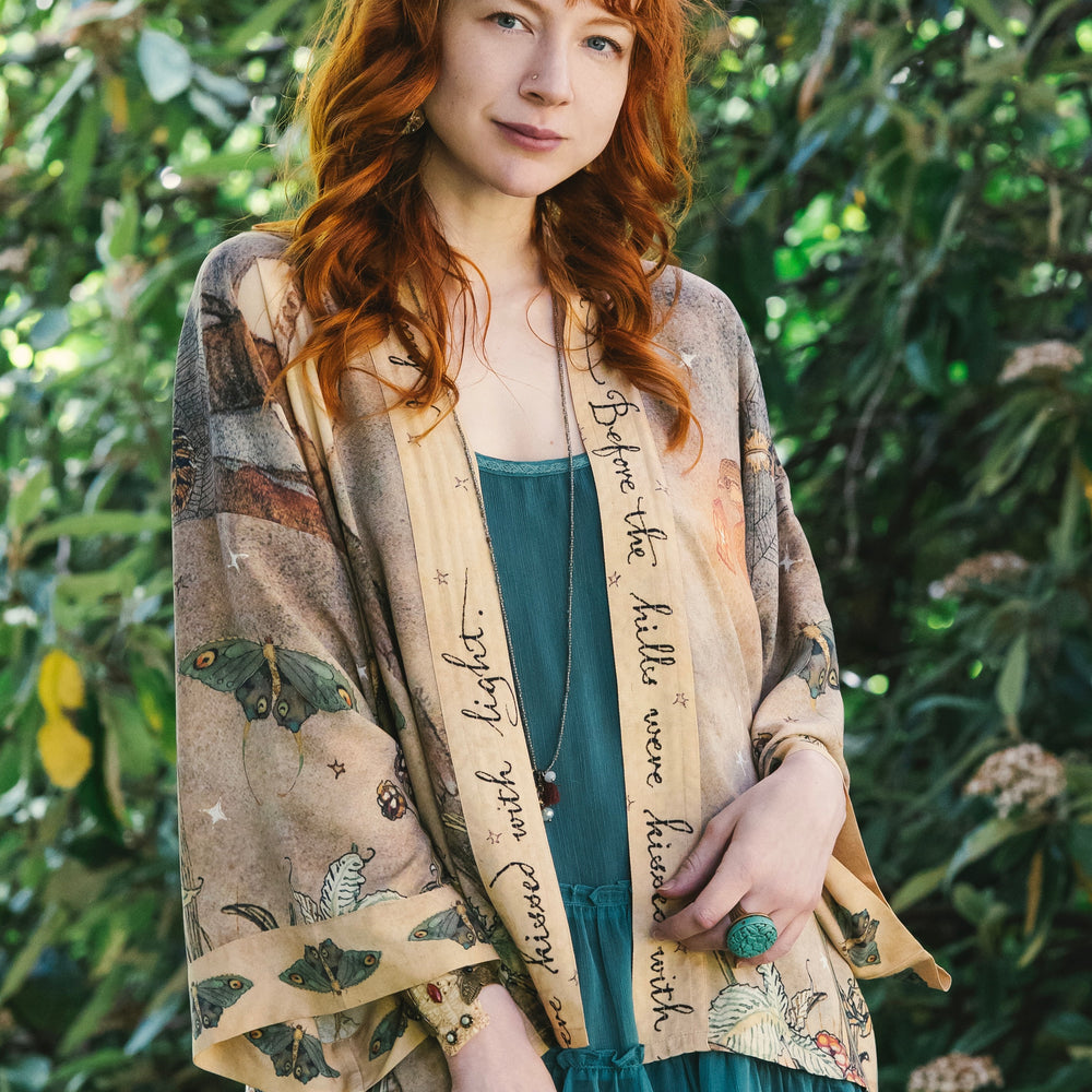 
                  
                    Model wearing an enchanting cropped kimono duster featuring illustrations by Charles van Sandwyck's, crafted from airy bamboo-based viscose with a touch of whimsical magic - Market of Stars
                  
                