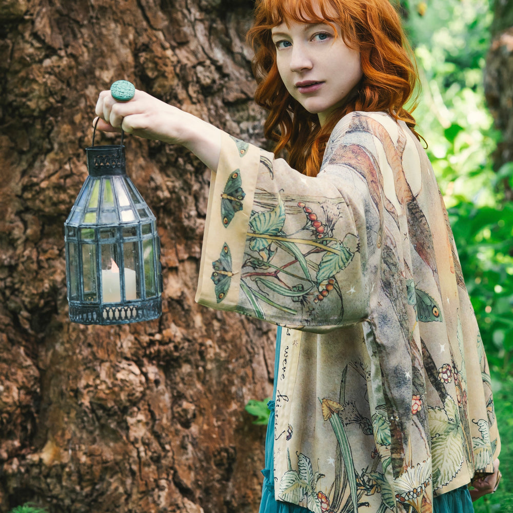 
                  
                    Model wearing an enchanting cropped kimono duster featuring illustrations by Charles van Sandwyck's, crafted from airy bamboo-based viscose with a touch of whimsical magic - Market of Stars
                  
                