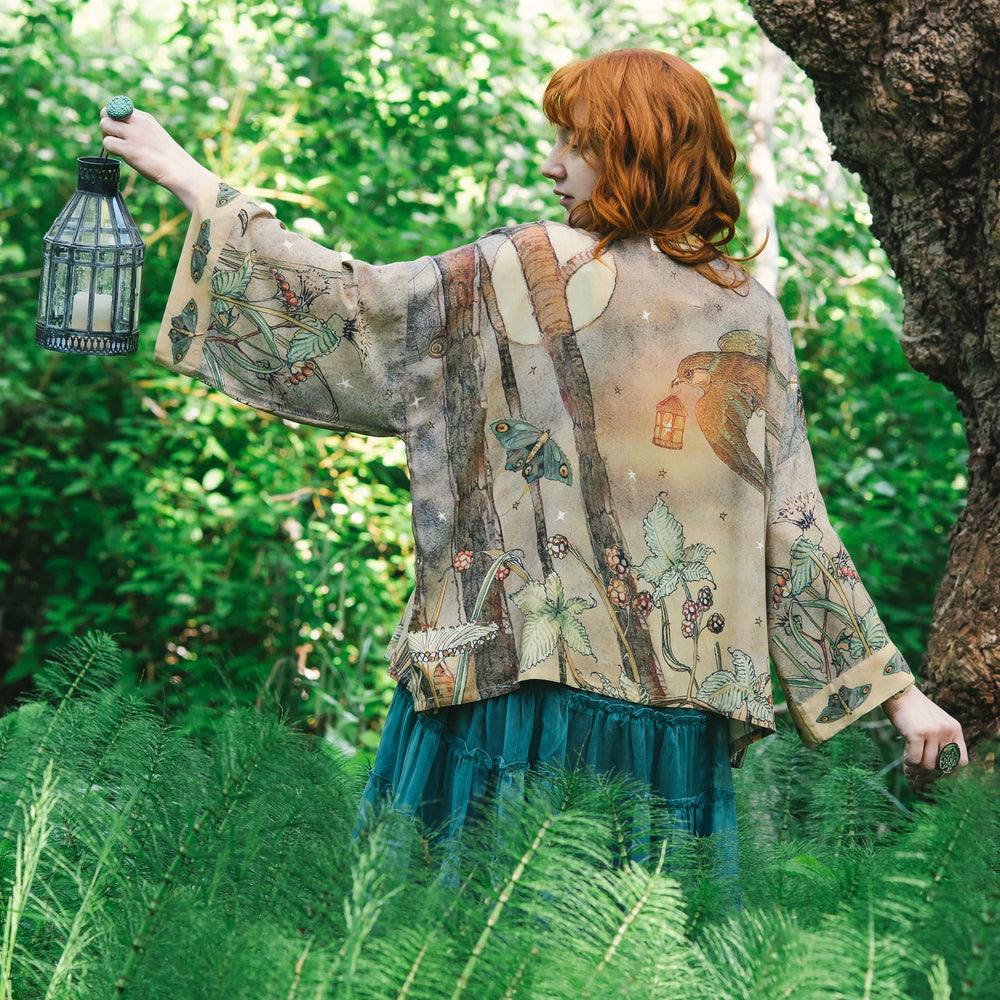 
                  
                    Model wearing an enchanting cropped kimono duster featuring illustrations by Charles van Sandwyck's, crafted from airy bamboo-based viscose with a touch of whimsical magic - Market of Stars
                  
                