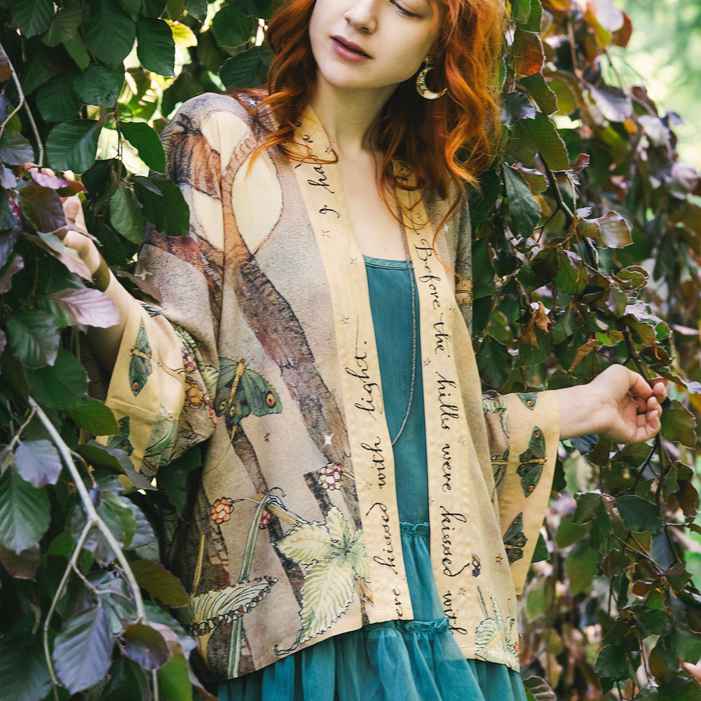 
                  
                    Model wearing an enchanting cropped kimono duster featuring illustrations by Charles van Sandwyck's, crafted from airy bamboo-based viscose with a touch of whimsical magic - Market of Stars
                  
                