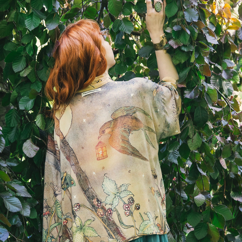 
                  
                    Model wearing an enchanting cropped kimono duster featuring illustrations by Charles van Sandwyck's, crafted from airy bamboo-based viscose with a touch of whimsical magic - Market of Stars
                  
                