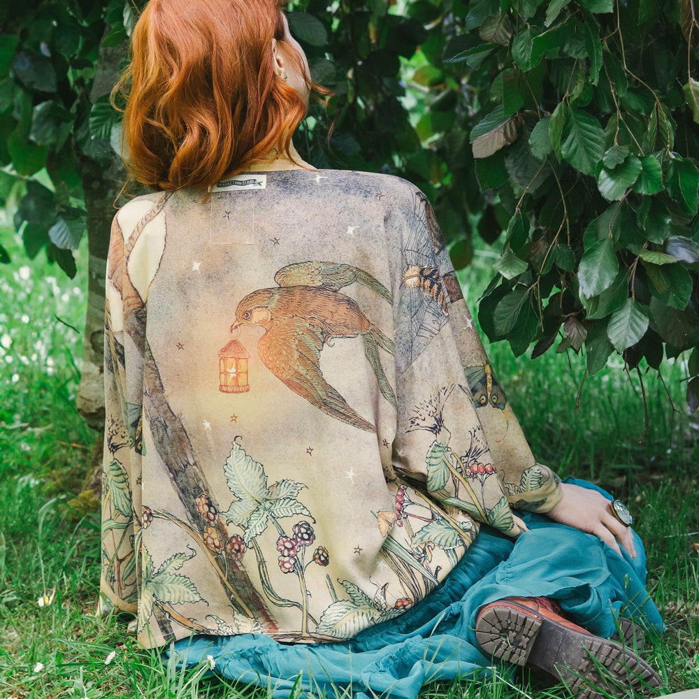 
                  
                    Model wearing an enchanting cropped kimono duster featuring illustrations by Charles van Sandwyck's, crafted from airy bamboo-based viscose with a touch of whimsical magic - Market of Stars
                  
                