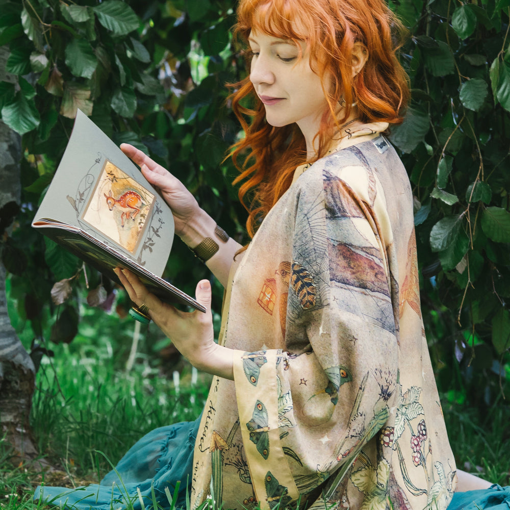 
                  
                    Model wearing an enchanting cropped kimono duster featuring illustrations by Charles van Sandwyck's, crafted from airy bamboo-based viscose with a touch of whimsical magic - Market of Stars
                  
                