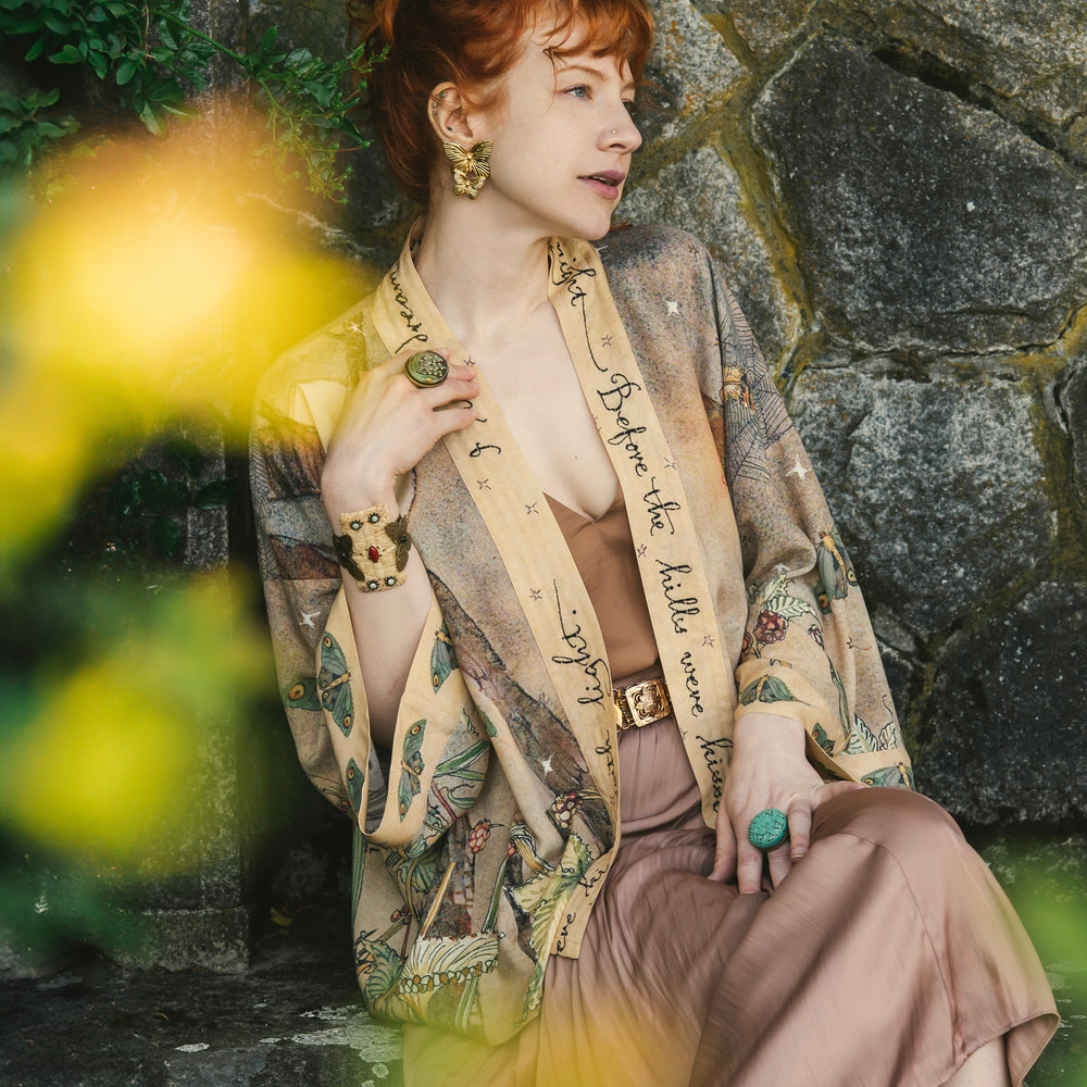 
                  
                    Model wearing an enchanting cropped kimono duster featuring illustrations by Charles van Sandwyck's, crafted from airy bamboo-based viscose with a touch of whimsical magic - Market of Stars
                  
                