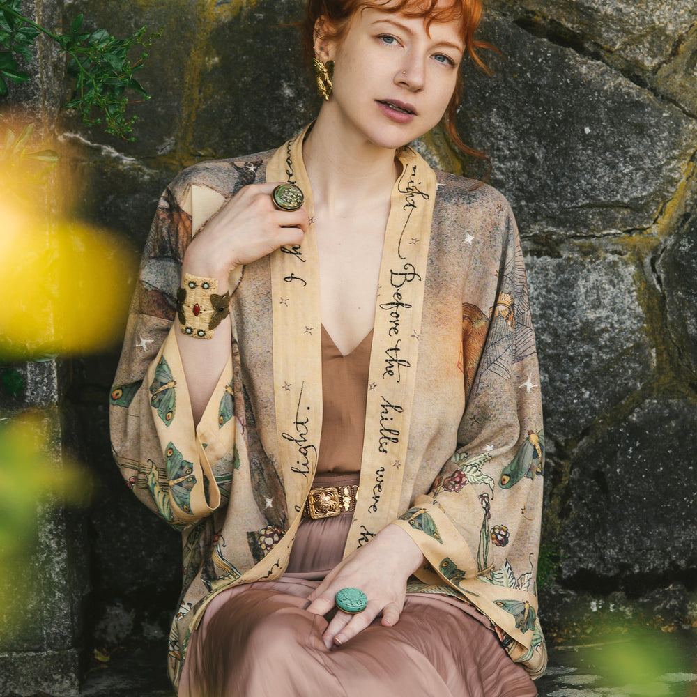 
                  
                    Model wearing an enchanting cropped kimono duster featuring illustrations by Charles van Sandwyck's, crafted from airy bamboo-based viscose with a touch of whimsical magic - Market of Stars
                  
                